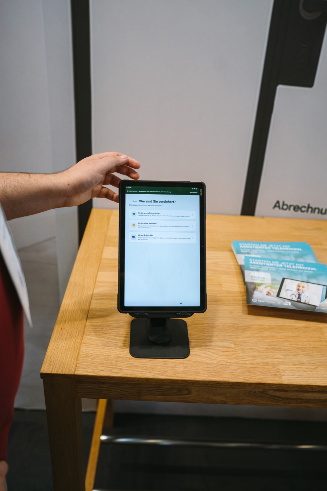 Demonstration am Care Tablet: eine Hand bedient die Ersteinschätzung auf dem Tischständer